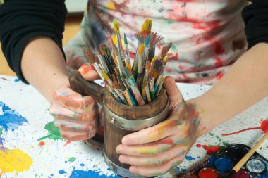 Boya paleti ve fırçalarla sanatçıların ellerine yakın çekim.