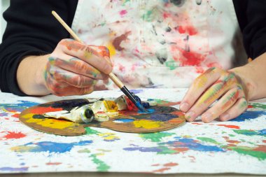 Boya paleti ve fırçalarla sanatçıların ellerine yakın çekim.