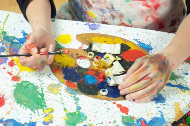 Boya paleti ve fırçalarla sanatçıların ellerine yakın çekim.