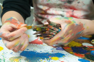 Boya paleti ve fırçalarla sanatçıların ellerine yakın çekim.