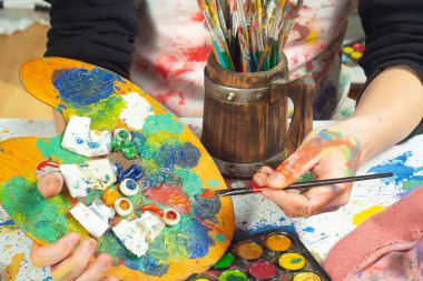 Boya paleti ve fırçalarla sanatçıların ellerine yakın çekim.