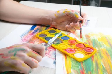 Boya paleti ve fırçalarla sanatçıların ellerine yakın çekim.