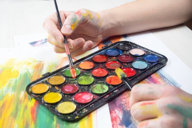 Boya paleti ve fırçalarla sanatçıların ellerine yakın çekim.