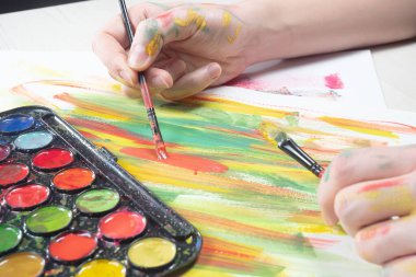 Boya paleti ve fırçalarla sanatçıların ellerine yakın çekim.