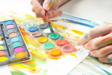 Boya paleti ve fırçalarla sanatçıların ellerine yakın çekim.