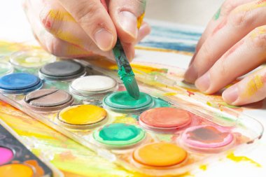 Boya paleti ve fırçalarla sanatçıların ellerine yakın çekim.