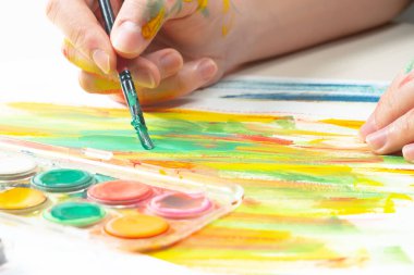 Boya paleti ve fırçalarla sanatçıların ellerine yakın çekim.