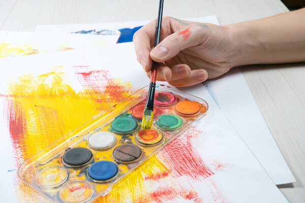 Крупный план рук художника с палитрой красок и кистей.