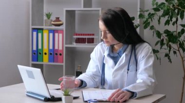 Genç, güzel bir bayan doktor bilgisayarında çalışıyor, belgelerdeki hasta sağlık verilerini kontrol ediyor ve veritabanına giriyor. Yavaş çekim.