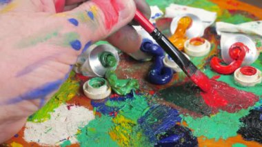 Sanatçının elleri, sanatta yaratıcı imgeler yaratmak için çalışır. Resim boyaları ve fırçalar, palet, guaj ve suluboya kullanarak tuvale çok renkli dokunuşlar uyguluyorlar..