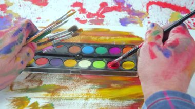 Sanatçının elleri, sanatta yaratıcı imgeler yaratmak için çalışır. Resim boyaları ve fırçalar, palet, guaj ve suluboya kullanarak tuvale çok renkli dokunuşlar uyguluyorlar..