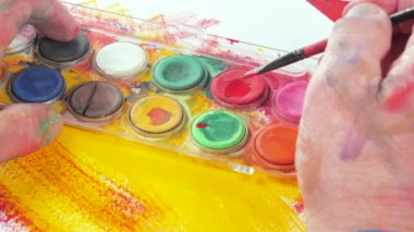 Sanatçının elleri, sanatta yaratıcı imgeler yaratmak için çalışır. Resim boyaları ve fırçalar, palet, guaj ve suluboya kullanarak tuvale çok renkli dokunuşlar uyguluyorlar..