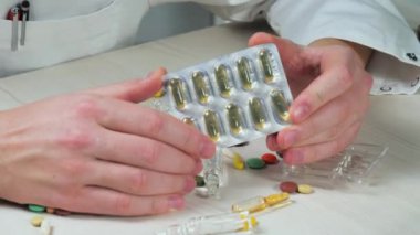 Genç bir doktor elinde hapları tutarken onları muayene ediyor. Elleri yakın çekim. Yavaş çekim.