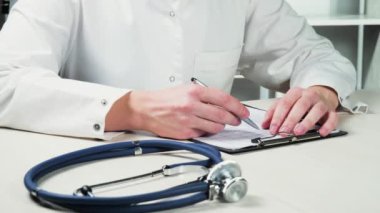 Genç bir doktor, hastanın tıbbi kayıtlarına yeni veriler yazıyor... yakın çekim. Yavaş çekim.