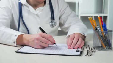 Genç bir doktor, hastanın tıbbi kayıtlarına yeni veriler yazıyor... yakın çekim. Yavaş çekim.