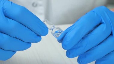 Genç bir doktor ampulün içindeki bir ilacı inceleyip kendi elleriyle çeviriyor. Eller yakın çekim. Yavaş çekim.