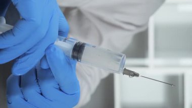 Mavi eldivenli doktor enjeksiyondan önce şırıngayı kontrol ederken iğneden sıkılan kan damlalar düşüyor. Eller yakın çekim. Yavaş çekim.