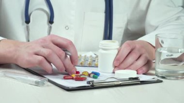 Ofisteki bir masada hapları inceleyen genç bir doktor. Eller yakın plan. Yavaş çekim.