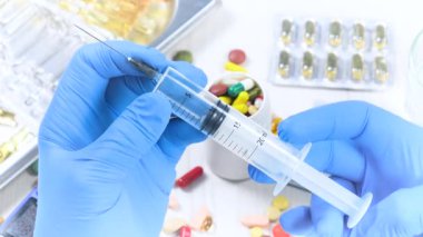 Mavi eldivenli genç doktor, enjeksiyondan önce şırıngayı kontrol ediyor. Yakın plan. Yavaş çekim.