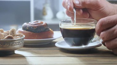 Yaşlı bir adamın elleri yavaşça sıcak espresso kahvesini kaşıkla karıştırıyor. Yavaş çekim.