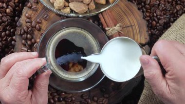 Yaşlı bir adamın elleri yavaşça kahveye süt döküyor. Yukarıdan bak. Yavaş çekim.