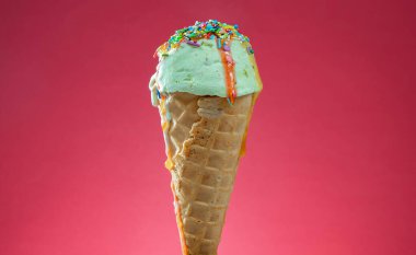 Kırmızı arka planda renkli serpiştirilmiş dondurma külahı. Kapat..