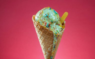 Kırmızı arka planda renkli serpiştirilmiş dondurma külahı. Kapat..