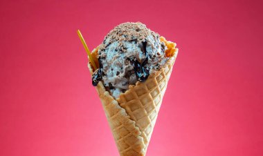 Kırmızı arka planda renkli serpiştirilmiş dondurma külahı. Kapat..