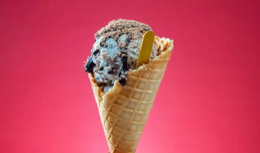 Kırmızı arka planda renkli serpiştirilmiş dondurma külahı. Kapat..