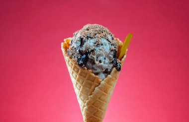 Kırmızı arka planda renkli serpiştirilmiş dondurma külahı. Kapat..