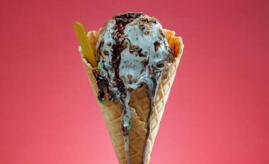 Kırmızı arka planda renkli serpiştirilmiş dondurma külahı. Kapat..