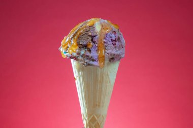 Kırmızı arka planda renkli serpiştirilmiş dondurma külahı. Kapat..