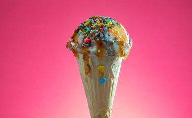 Kırmızı arka planda renkli serpiştirilmiş dondurma külahı. Kapat..