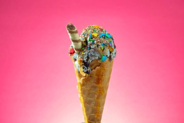 Kırmızı arka planda renkli serpiştirilmiş dondurma külahı. Kapat..