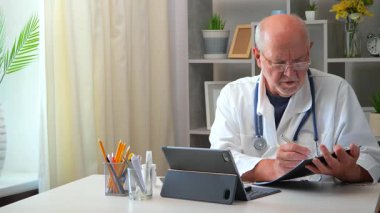 Yaşlı bir erkek doktor, doktorluk yapıyor, belgelerle uğraşıyor, hastalarla iletişim kuruyor, teşhis koyuyor, tedavi uyguluyor. Yavaş çekim.