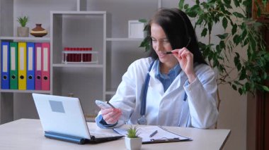 Genç bir kız, bir doktor, tıbbi pratikte çalışıyor, belgelerle çalışıyor, hastalarla iletişim kuruyor, teşhis koyuyor, tedavi oluyor, gülümsüyor. Yavaş çekim.