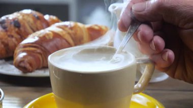 Yaşlı bir adamın elleri yavaşça sıcak espresso kahvesini kaşıkla karıştırıyor. Yavaş çekim.