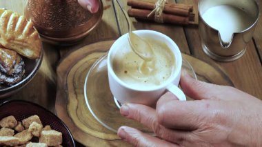 Yaşlı bir adamın elleri yavaşça sıcak espresso kahvesini kaşıkla karıştırıyor. Yavaş çekim.