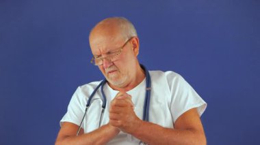 Yaşlı bir doktor, mavi arka planda, etrafa bakıyor. Yavaş çekim.