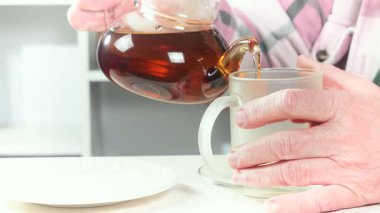 Çay içmeden önce çaydanlıktan bir fincana çay dolduran yaşlı bir adamın elleri. Yakın plan. Yavaş çekim.