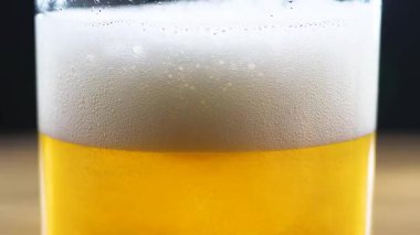 Hafif, köpüklü bira, dolu bir bardakta, dönen, köpüklü hava kabarcıkları. Yakın plan. Yavaş çekim.
