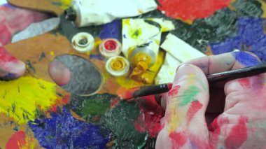 Sanatçının elleri, sanatta yaratıcı imgeler yaratmak için çalışır. Resim boyaları ve fırçalar, palet, guaj ve suluboya kullanarak tuvale çok renkli dokunuşlar uyguluyorlar..