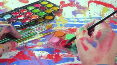 Sanatçının elleri, sanatta yaratıcı imgeler yaratmak için çalışır. Resim boyaları ve fırçalar, palet, guaj ve suluboya kullanarak tuvale çok renkli dokunuşlar uyguluyorlar..