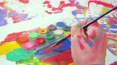 Sanatçının elleri, sanatta yaratıcı imgeler yaratmak için çalışır. Resim boyaları ve fırçalar, palet, guaj ve suluboya kullanarak tuvale çok renkli dokunuşlar uyguluyorlar..