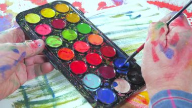 Sanatçının elleri, sanatta yaratıcı imgeler yaratmak için çalışır. Resim boyaları ve fırçalar, palet, guaj ve suluboya kullanarak tuvale çok renkli dokunuşlar uyguluyorlar..