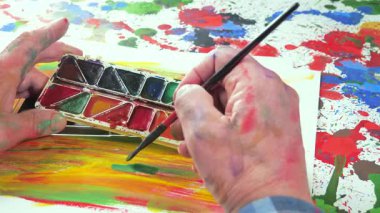 Sanatçının elleri, sanatta yaratıcı imgeler yaratmak için çalışır. Resim boyaları ve fırçalar, palet, guaj ve suluboya kullanarak tuvale çok renkli dokunuşlar uyguluyorlar..