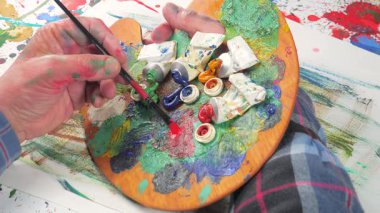 Sanatçının elleri, sanatta yaratıcı imgeler yaratmak için çalışır. Resim boyaları ve fırçalar, palet, guaj ve suluboya kullanarak tuvale çok renkli dokunuşlar uyguluyorlar..