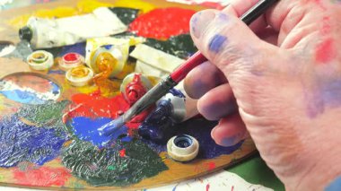 Sanatçının elleri, sanatta yaratıcı imgeler yaratmak için çalışır. Resim boyaları ve fırçalar, palet, guaj ve suluboya kullanarak tuvale çok renkli dokunuşlar uyguluyorlar..