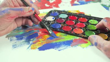 Sanatçının elleri, sanatta yaratıcı imgeler yaratmak için çalışır. Resim boyaları ve fırçalar, palet, guaj ve suluboya kullanarak tuvale çok renkli dokunuşlar uyguluyorlar..