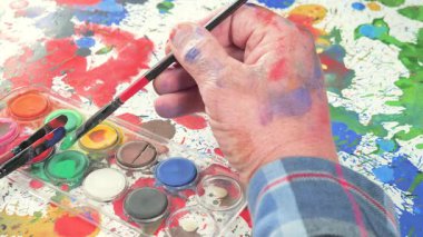 Sanatçının elleri, sanatta yaratıcı imgeler yaratmak için çalışır. Resim boyaları ve fırçalar, palet, guaj ve suluboya kullanarak tuvale çok renkli dokunuşlar uyguluyorlar..